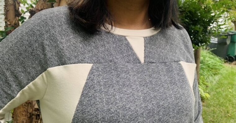 Close-up of a woman wearing a grey Noord Sweatshirt with cream color blocking at neck and sides