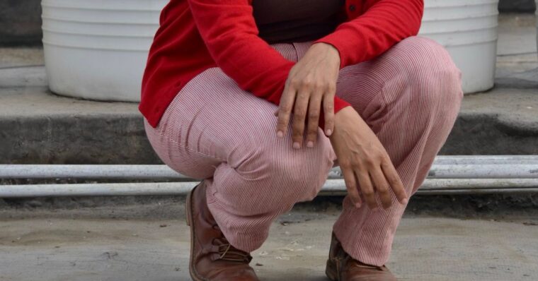 Close up of woman crouching in red and white trousers, wearing a brown sweater and a red cardigan.